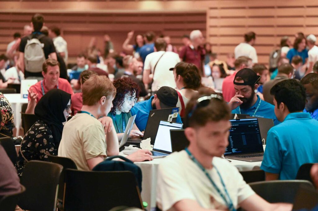 A busy conference room with people working on laptops and engaging in discussions.