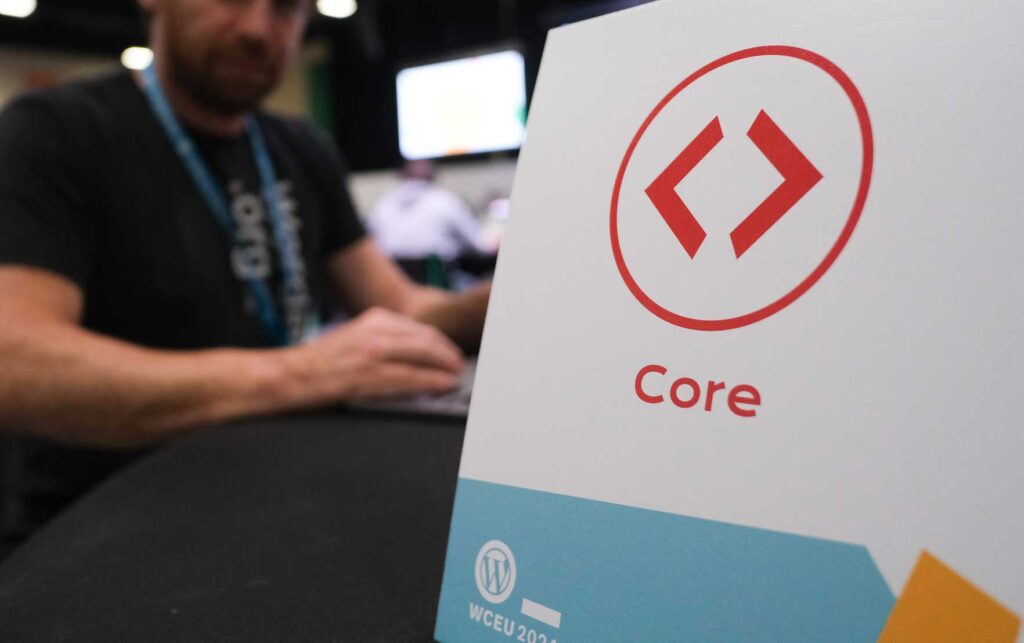A sign with the word "Core" and a logo, with a blurred person typing in the background.