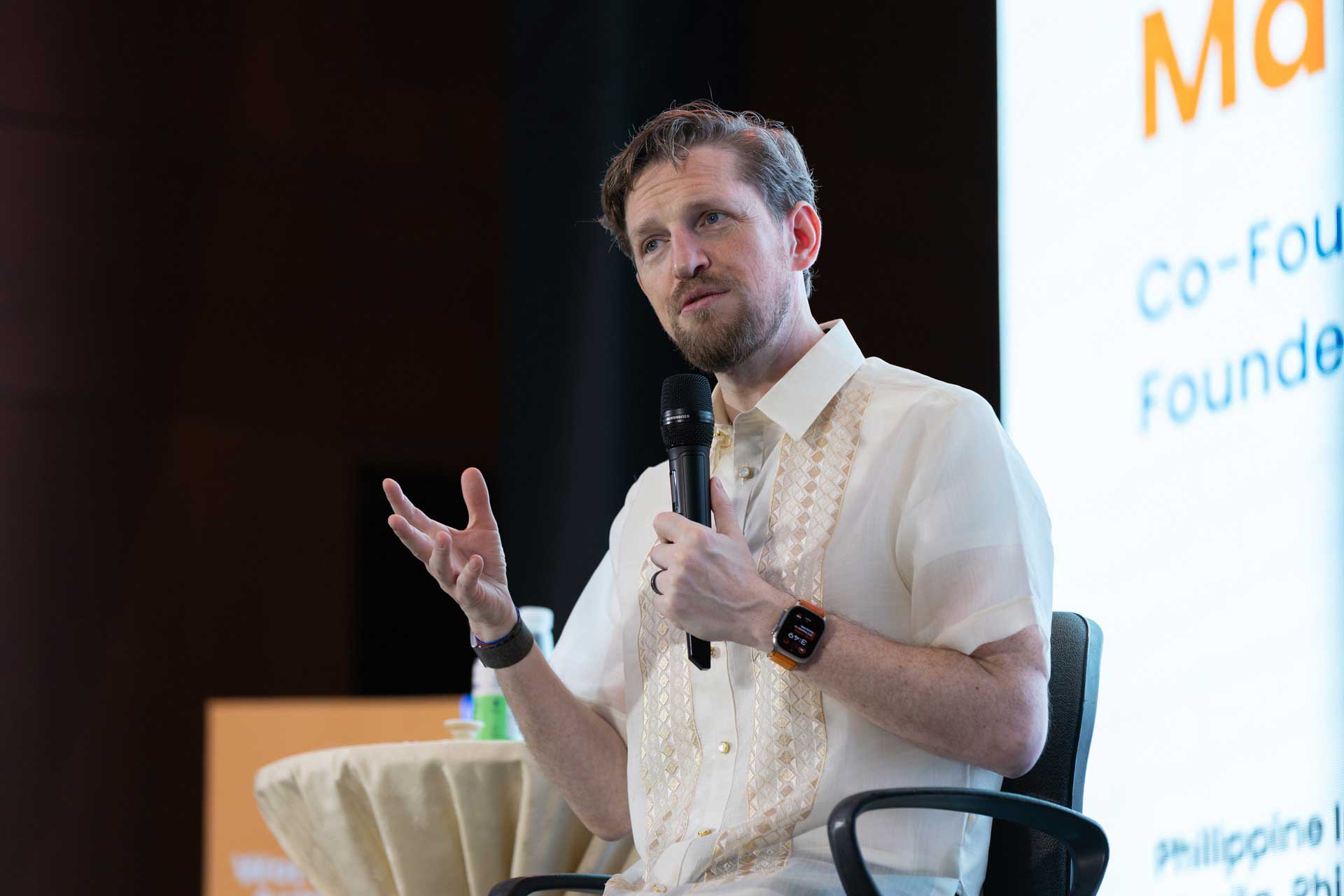 A man in a traditional Filipino barong speaks into a microphone during an event.