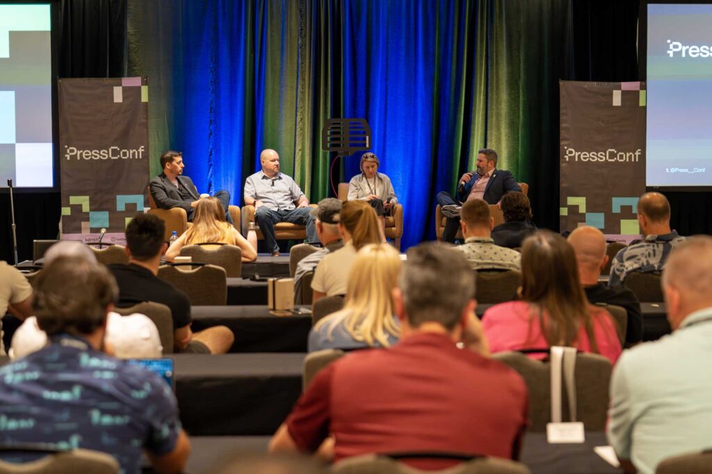 Panel discussion at a conference with speakers on stage and an audience in view.
